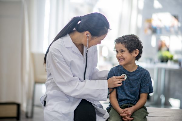 Young boy smiles while female healthcare provider checks him with a stethoscope